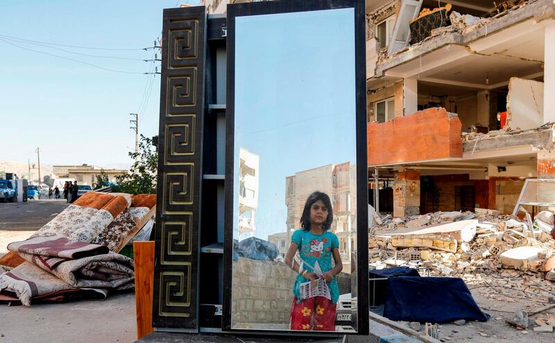 TOPSHOT - An Iranian girl looks through a salvaged mirror from a damaged building in the town of Sarpol-e Zahab in the western Kermanshah province near the border with Iraq, on November 14, 2017, following a 7.3-magnitude earthquake that left hundreds killed and thousands homeless two days before. / AFP PHOTO / ATTA KENARE