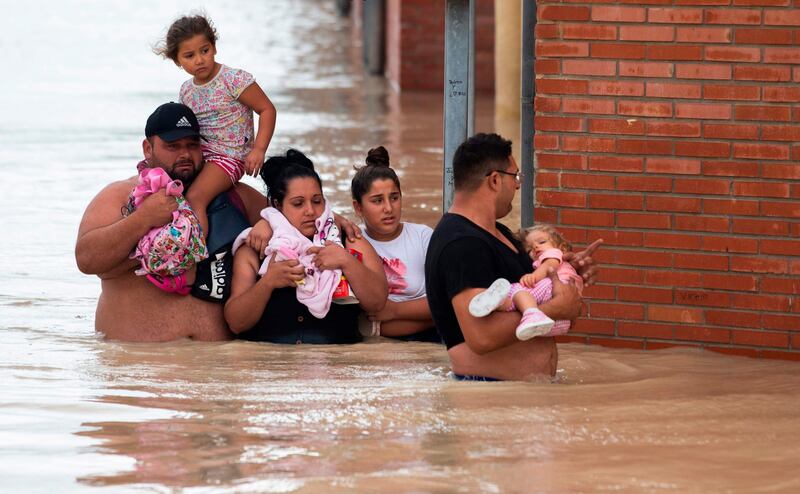 Peolple carry children on a flooded street in Almoradi on September 13, 2019. Two more people died as torrential rain and flash floods battered southeastern Spain, raising the death toll to four as the storm caused havoc for travellers and forced 3,500 people from their homes. / AFP / JOSE JORDAN

