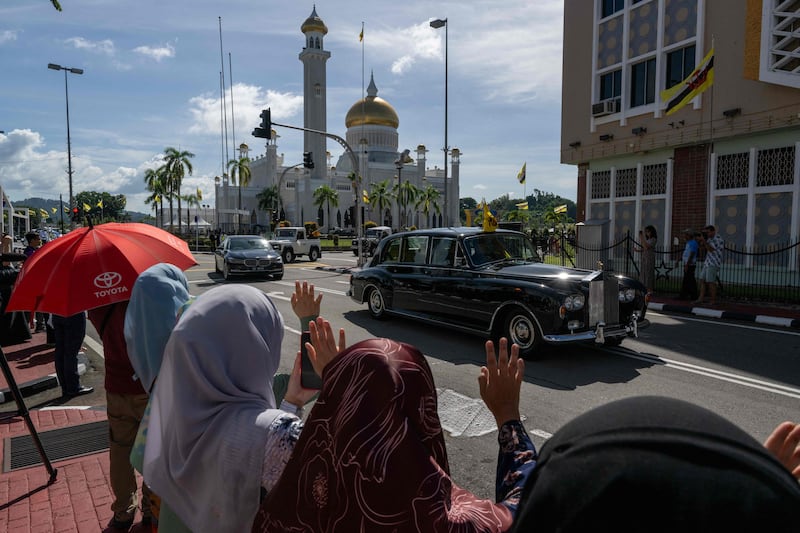 People take to the streets to wave as Sultan Hassanal Bolkiah passes by. AFP