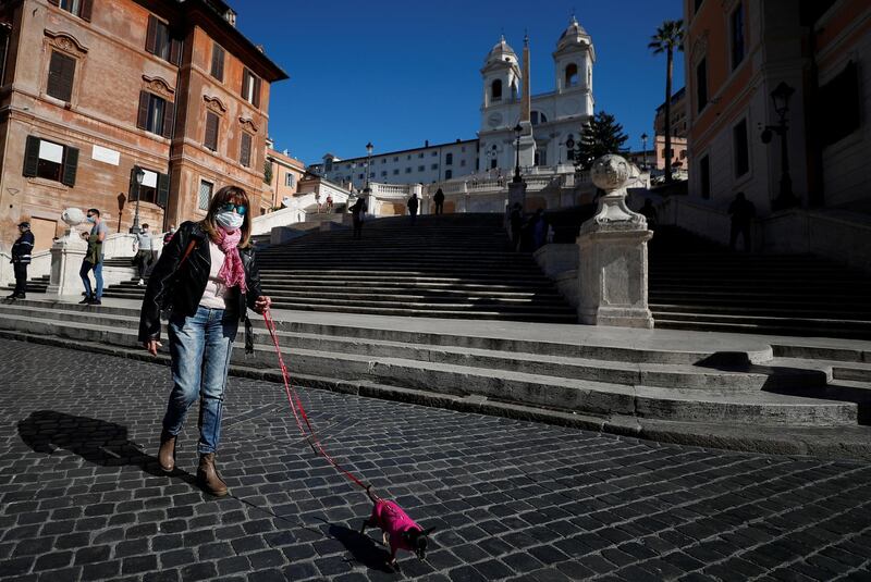 A woman wears a face mask as she walks a dog in Rome, Italy. Reuters