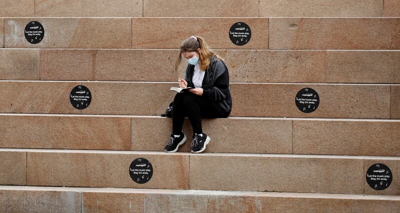 A woman reads a book while sitting between social distancing markers in Liverpool.