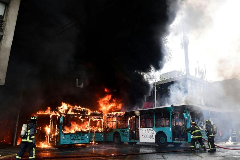 TOPSHOT - Chilean firefighters extinguish burning buses during clashes between protesters and the riot police in Santiago, on October 19, 2019. Chile's president declared a state of emergency in Santiago Friday night and gave the military responsibility for security after a day of violent protests over an increase in the price of metro tickets. / AFP / Martin BERNETTI
