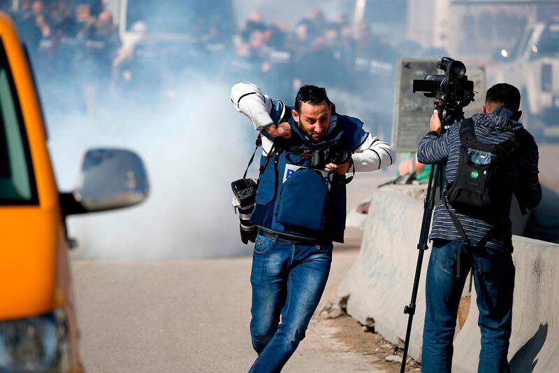 Journalists run as tear gas is fired by Israeli forces during a march in the occupied West Bank. AFP