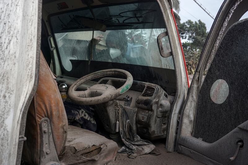 A villager checks on a car covered by volcanic ash. EPA