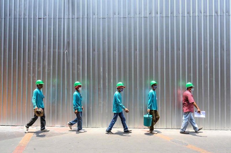 Construction workers wearing face masks and keeping safe distance walk on a street in Bangkok.  AFP