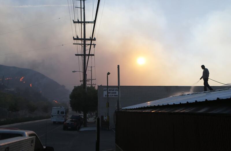 A man uses a garden hose to water down a rooftop as the Tick Fire burns nearby in Canyon Country. AFP