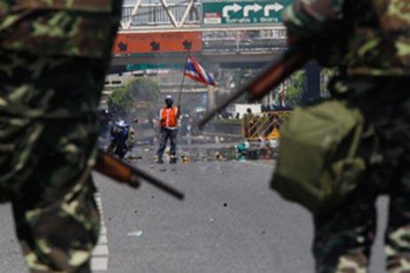 An anti-government demonstrator holds a Thai flag in front of soldiers at a main street in central Bangkok today.