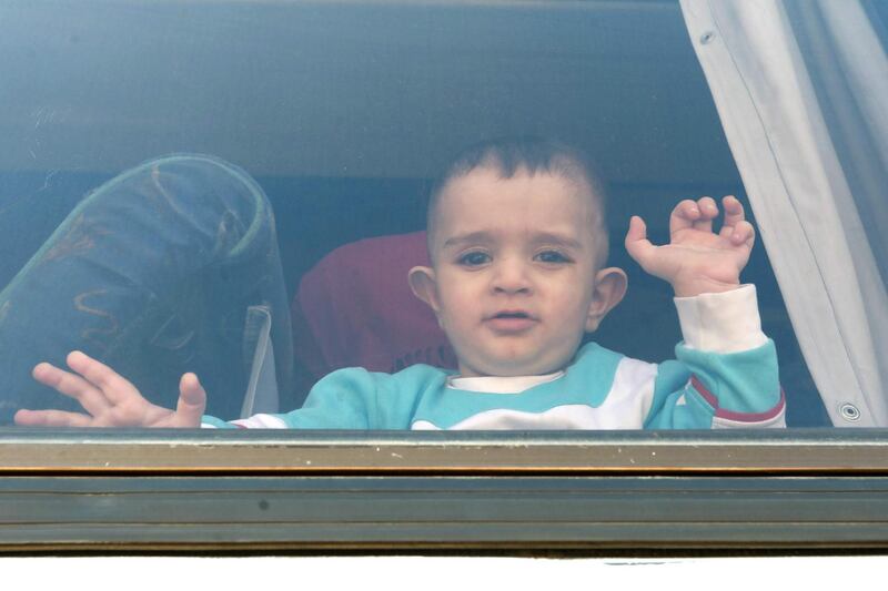 A Syrian toddler refugee waves through the windows of a bus as it leaves Beirut. AFP