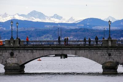 Eastern Swiss Alps are seen in the background as people cross the Limmat River on the Muensterbruecke bridge, as the spread of the coronavirus disease (COVID-19) continues, in Zurich, Switzerland March 13, 2021. REUTERS/Arnd Wiegmann