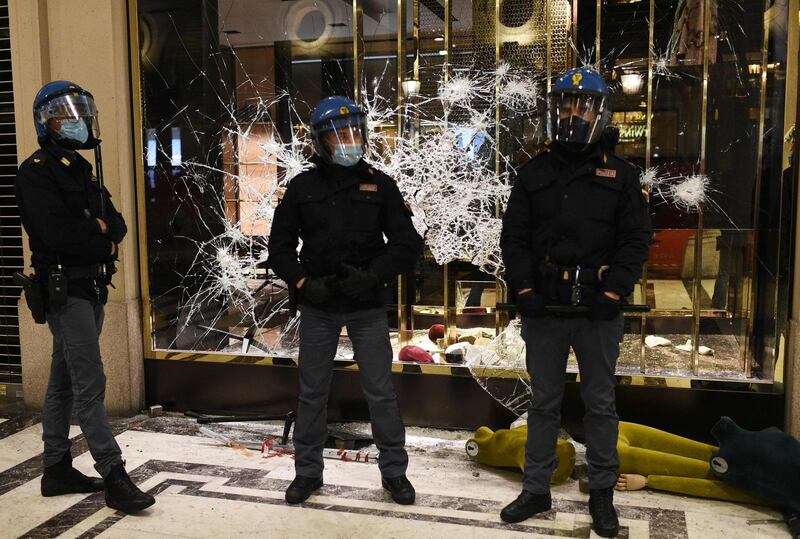 Italian police officers stand in front of a shattered Gucci store window during a protest of far-right activists against the government restriction measures to curb the spread of COVID-19, in downtown Turin, on October 26, 2020, as the country faces a second wave of infections to the Covid-19 (the novel coronavirus). Italy's Prime Minister Giuseppe Conte tightened nationwide coronavirus restrictions on October 25, 2020 after the country registered a record number of new cases, despite opposition from regional heads and street protests over curfews. Cinemas, theatres, gyms and swimming pools must all close under the new rules, which come into force on October 26, 2020 and run until November 24, while restaurants and bars will stop serving at 6pm, the prime minister's office said. / AFP / Marco BERTORELLO                    
