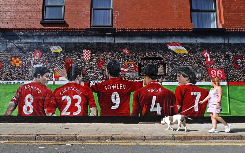 A woman walks her dog past a mural on the side of a hotel depicting Liverpool football club former players Steven Gerrard, Jamie Carragher, Robbie Fowler, current defender Virgil van Dijk and former player and manager Kenny Dalglish in Anfield, Liverpool, England. AFP