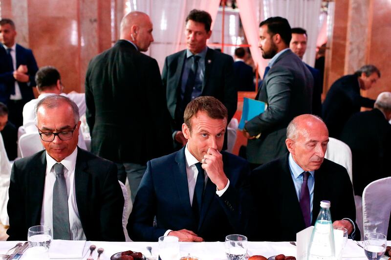 Elysee senior security officer Alexandre Benalla appears in the background as French President Emmanuel Macron (C) and French Interior Minister Gerard Collomb (R) attend a dinner organised by the French Council of the Muslim Faith (CFCM) to break the fast of Ramadan in Paris on June 20, 2017. Alexandre Benalla, 26, is at the centre of an escalating scandal for the French president after being filmed assaulting a protester during a May Day demonstration, and following media reports that the assault was kept quiet.   / AFP / Benjamin CREMEL
