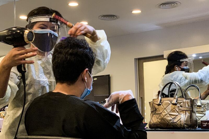 A hairdresser clad in face shield and mask blow-dries a client's hair at a women's salon in Saudi Arabia's capital Riyadh.   AFP