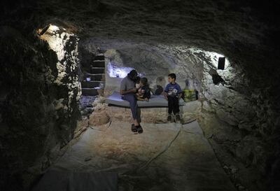TOPSHOT - Syrian Hadheefa al-Shahadh, 27, sits with his children in a cave that he dug inside his house to shelter him and his family as part of preparations for any upcoming raids in the rebel-held Idlib province's village of Maar Shurin, on September 11, 2018. - Fearing government forces and their allies military advance to retake Idlib province, the father of three learnt from YouTube videos how to make gas masks from charcoal, wood, paper cups, cotton, nylon plastic bags and tapes. According to him, he could manufacture more masks but the material he needs are not always available. (Photo by OMAR HAJ KADOUR / AFP)