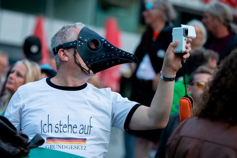 A man with a beak mask holds a camera at a rally against coronavirus measures on Thursday, August 27, 2020. The rally was a prelude to a demonstration expected on Saturday. Police in Berlin have requested thousands of reinforcements from other parts of Germany to cope with planned protests at the weekend by people opposed to coronavirus restrictions. dpa via AP
