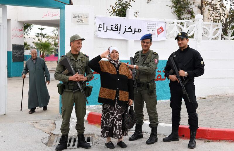 A Tunisian woman holds up her right hand in a gesture of salute as she stands between army soldiers standing on guard outside a polling station in Ben Arous near the capital Tunis, during the first free municipal elections since the 2011. Fethi Belaid / AFP