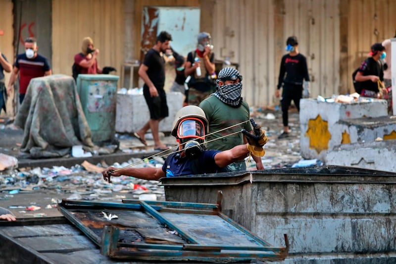 A protester aims a slingshot with a stone at police, during clashes between Iraqi security forces and anti-government demonstrators in downtown Baghdad. AP Photo