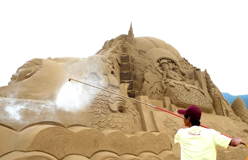 A worker sprays glue onto a sand sculpture. AFP