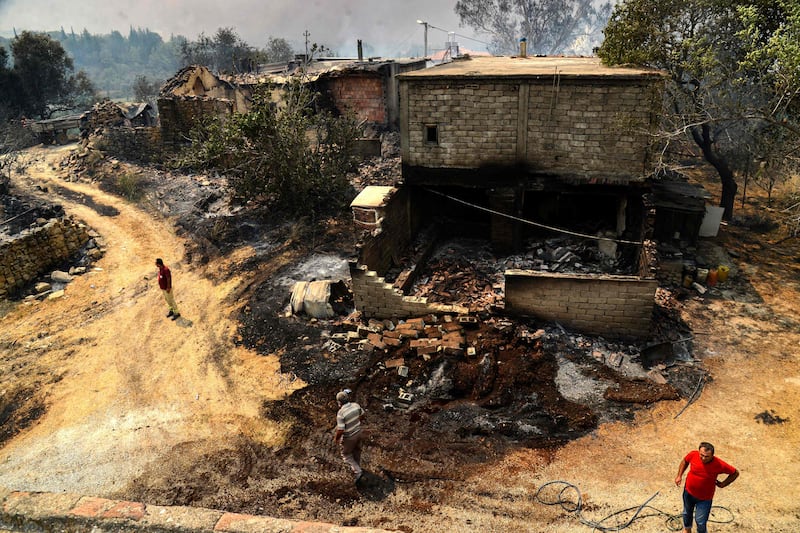 People stand next to a burnt house during a large bushfire near the town of Manavgat.