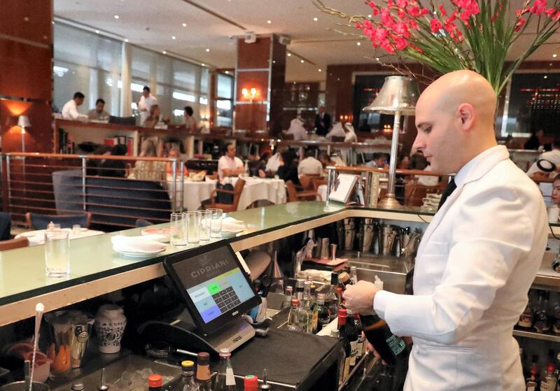 A bar tendant serves customers at a restaurant in Dubai on August 30, 2018. - As temperature levels soar in Dubai, residents and tourists in the rich Emirate turn to a much favourite indoor outing during summer days: restaurants. From ‚Äúbusiness lunches‚Äù, to fresh decorations, Dubai‚Äôs top restaurants compete to attract those costumers looking to beat the heat with a customised cool drink, or an award winning plate. (Photo by KARIM SAHIB / AFP)