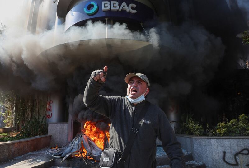A demonstrator gestures near a bank, set on fire, during a protest organized by Depositors' Outcry, a group campaigning for angry depositors, against informal restrictions on cash withdrawals and deteriorating economic conditions in Beirut, Lebanon February 16, 2023.  REUTERS / Mohamed Azakir