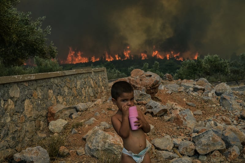 A child stands in his family's yard as a wildfire burns nearby, in the village of Agios Charalampos near Athens, in July 2023. Europe saw record temperatures amid a relentless heatwave and wildfires that scorched vast regions of the Northern Hemisphere, forcing the evacuation of 1,200 children close to a Greek seaside resort. Health authorities sounded alarms from North America to Europe and Asia, urging people to stay hydrated and shelter from the burning sun, in a stark reminder of the effects of global warming. AFP