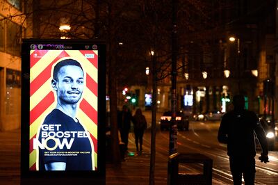 Pedestrians walk past a government ad promoting the NHS Covid-19 vaccine Booster programme in the centre of Manchester on December 31, 2021. AFP