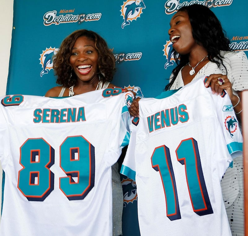 Serena, left, and Venus Williams pose for photo while displaying their Miami Dolphins jerseys after it was announced the tennis stars had become minority owners of the NFL football team, during a news conference in Davie, Fla., Tuesday, Aug. 25, 2009. (AP Photo/J Pat Carter)