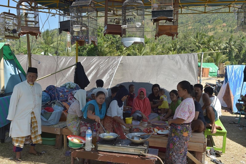 Women prepare meals underneath songbirds kept in cages at a temporary shelter in Pemenang, Northern Lombok.  AFP
