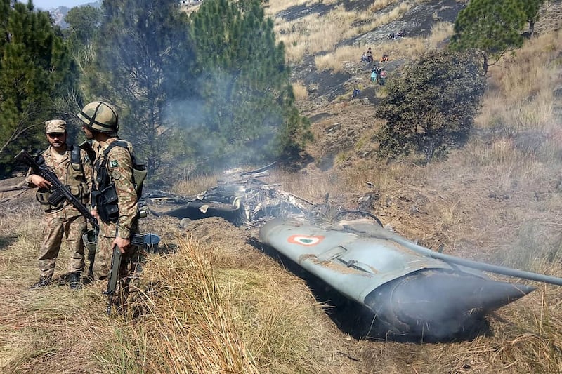 TOPSHOT - Pakistani soldiers stand next to what Pakistan says is the wreckage of an Indian fighter jet shot down in Pakistan controled Kashmir at Somani area in Bhimbar district near the Line of Control on February 27, 2019. Pakistan said on February 27 it shot down two Indian warplanes in its airspace over disputed Kashmir, in a dramatic escalation of a confrontation that has ignited fears of an all-out conflict between the nuclear-armed neighbours. / AFP / STR
