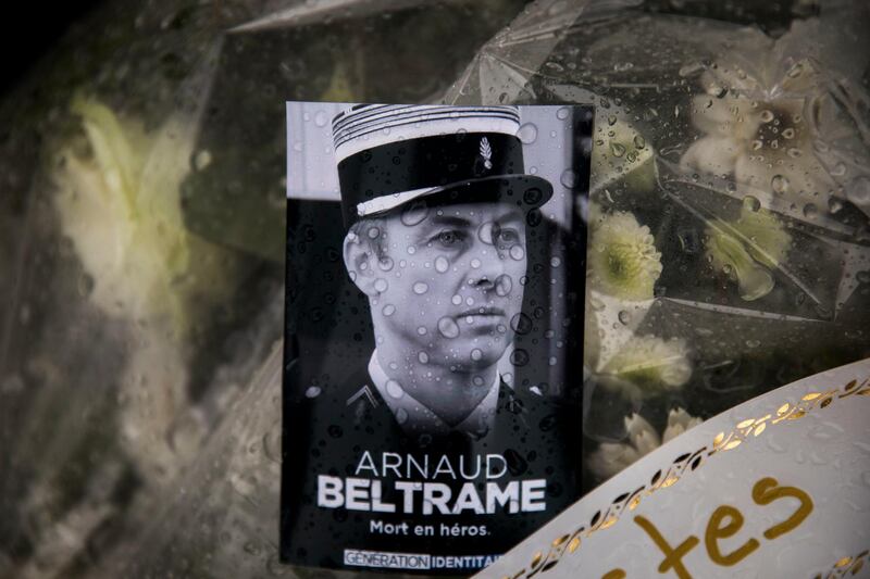 A photo of Lieutenant Colonel Arnaud Beltrame placed on a bunch of flowers at the main gate of the Police headquarters in Carcassonne, France, Saturday, March 24, 2018, following an attack on a supermarket in Trebes in the south of the country on Friday. A French police officer who offered himself up to an Islamic extremist gunman in exchange for a hostage died of his injuries, raising the death toll in the attack to four, and the officer was honored Saturday as a national hero of "exceptional courage and selflessness." (AP Photo/Emilio Morenatti)