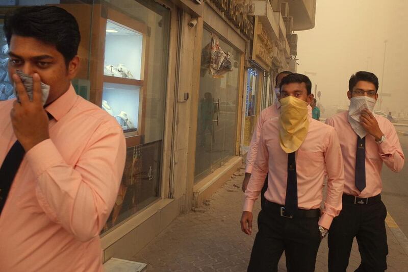 Office workers cover their noses and mouths during the sandstorm in Abu Dhabi. Delores Johnson / The National 