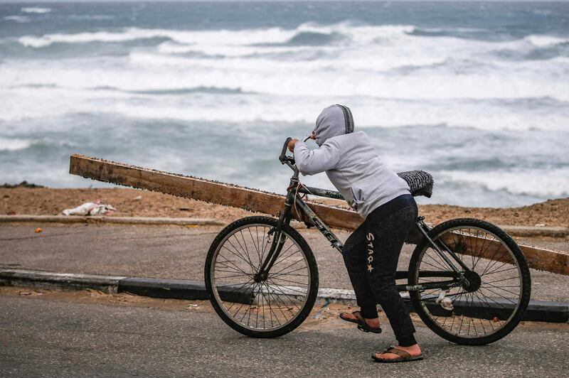 A Palestinian boy pushes a bicycle laden with a wooden beam along the Mediterranean seashore during stormy weather in Gaza. AFP