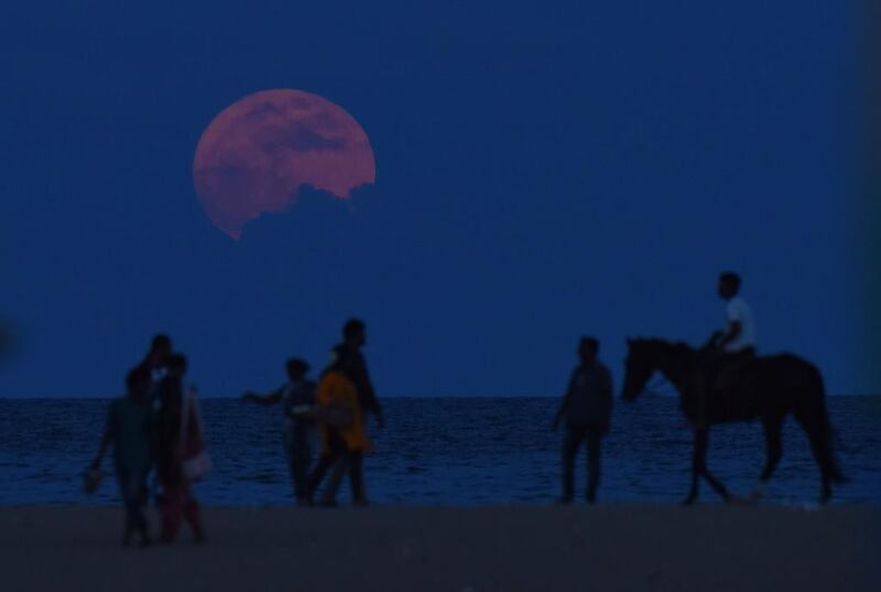 A man rides a horse past people watching the supermoon rise at Marina Beach in Chennai. Arun Sankar / AFP Photo