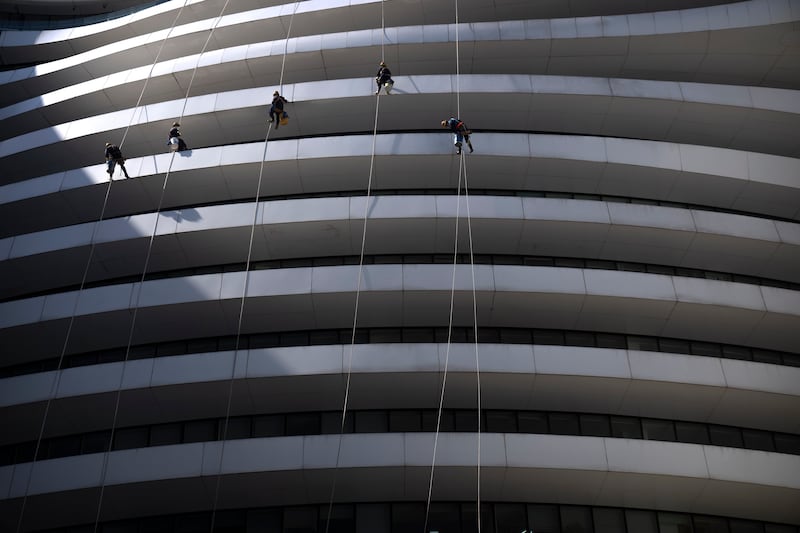 Window cleaners hang from the side of an office building in Beijing. AP Photo