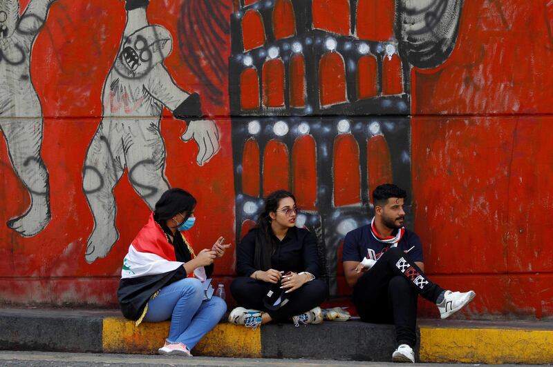 Demonstrators sit in front of a mural painted by anti-government protesters in Baghdad. Reuters