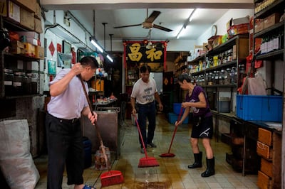 Shop owners clean their shop after a storm surge caused flooding, a day after Typhoon Mangkhut hit Macau on September 17, 2018. / AFP / ISAAC LAWRENCE
