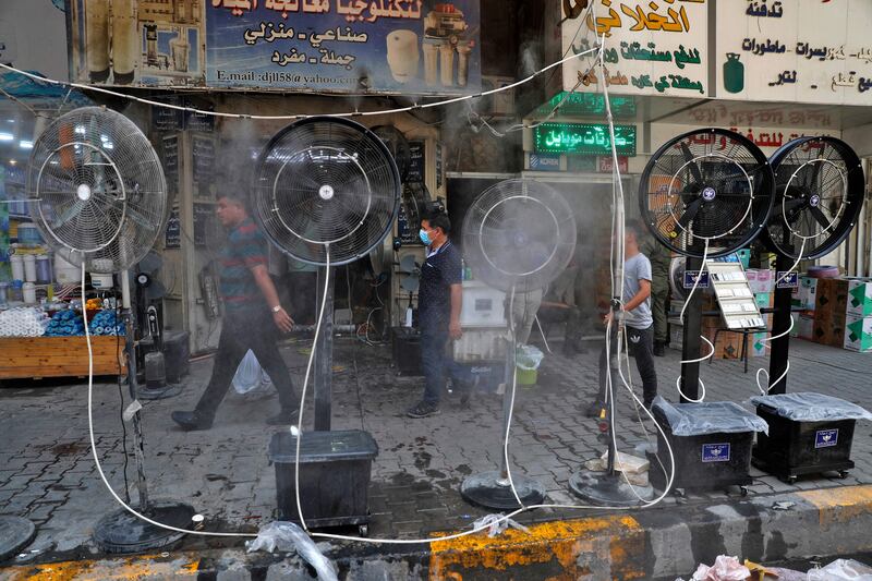Pedestrians in Baghdad enjoy the cooling spray from fans blowing air mixed with water into a Baghdad street during a heat wave.
