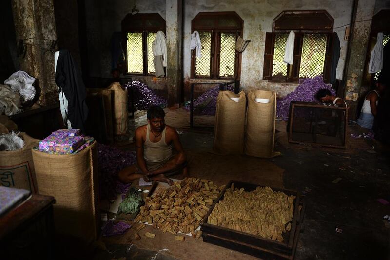 A young labourer looks on as he sits in near darkness packing bidis into colourful conical packets and boxes at The New Sarkar Bidi Factory in Kannauj.