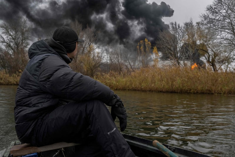 A fisherman sails his boat on the Dnipro as black smoke rises from an oil reserve in Kherson. AFP