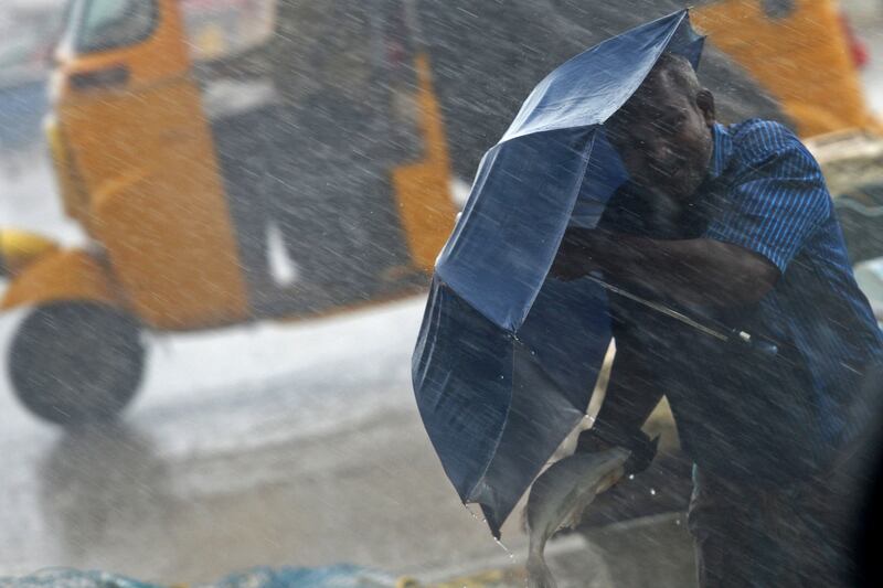 A vendor holds an umbrella while waiting for customers at a fish market during a heavy rainstorm in Chennai, India. AFP