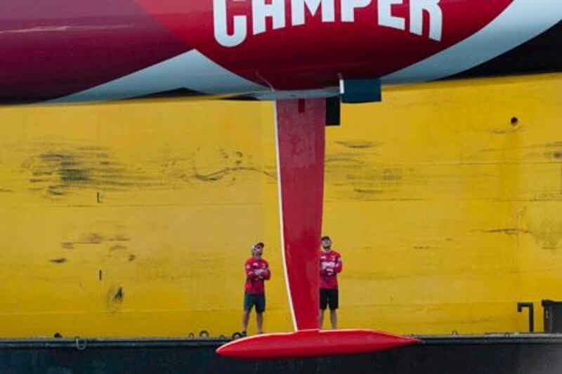 Two of Camper/Emirates Team New Zealand crew members watch as the Volvo Open 70-class sailing yacht is hoisted aboard a cargo vessel to be shipped to Sharjah.