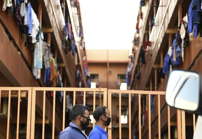 Foreign workers wearing protective masks amid the COVID-19 pandemic, walk past a worker housing complex in Dubai's Qusais neighbourhood, in the United Arab Emirates, on May 1, 2020, marking International Workers' Day (Labour Day). / AFP / Karim SAHIB
