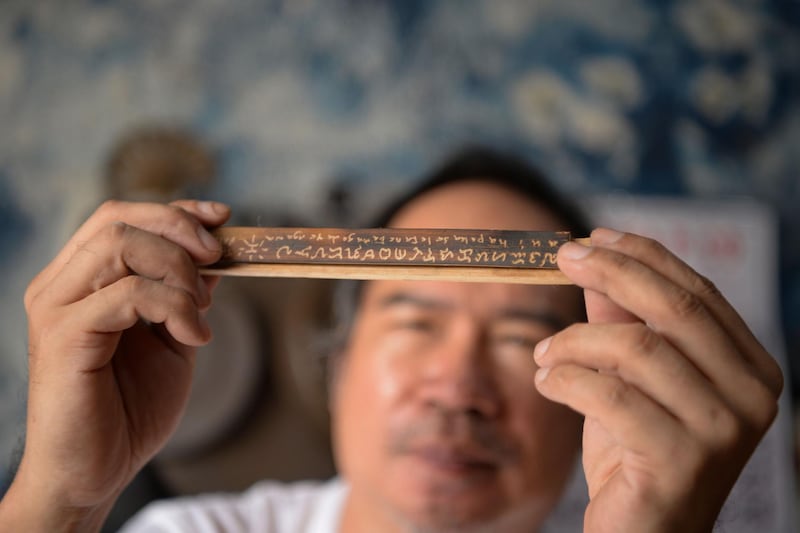 This photo taken on June 11, 2019 shows cultural advocate Leo Emmanuel Castro holding a piece of bamboo inscribed with indigenous Baybayin script at his shop in Manila.  From tattoos, shirts, and artworks to a computer font and mobile apps, Baybayin found a rebirth among millennials and professionals learning its 17 characters beyond the marginal mention in history class.