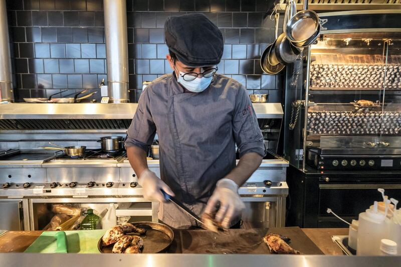 DUBAI, UNITED ARAB EMIRATES. 08 JUNE 2020. Staff at Nightjar Coffee in Al Serkal Avenue, Al Quoz follow strict sanitary procedures due to the current COVID-19 Pandemic to ensure health and safety measures put in place by Dubai Municipality is adhered to. A chef prepares freshly roasted chicken wearing a face mask and gloves. (Photo: Antonie Robertson/The National) Journalist: None. Section: National.