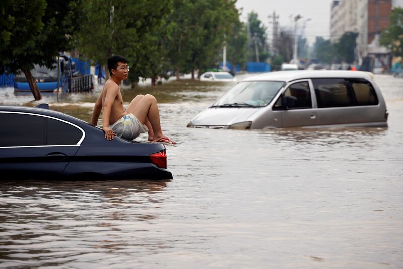 A man sits on his stranded car as the floodwater rises.