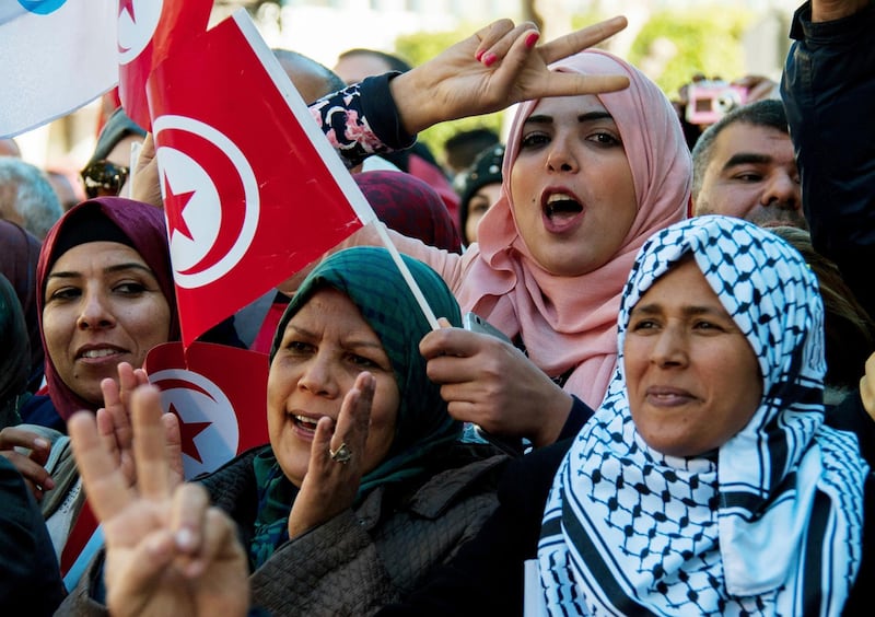 A Tunisian woman holds the national flag and make a sign during a rally to mark seven years since revolution in Tunis, Tunisia, Sunday, Jan. 14, 2018. Tunisian authorities announced plans to boost aid to the needy in a bid to placate protesters whose demonstrations over price hikes degenerated into days of unrest across the North African nation, which is marking seven years on Sunday since its long-time autocratic ruler was driven into exile. (AP Photo/Hassene Dridi)