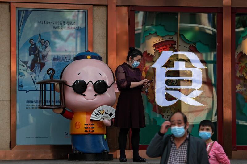 People wearing face masks walk by a worker using her smartphone outside a restaurant in Beijing. AP Photo