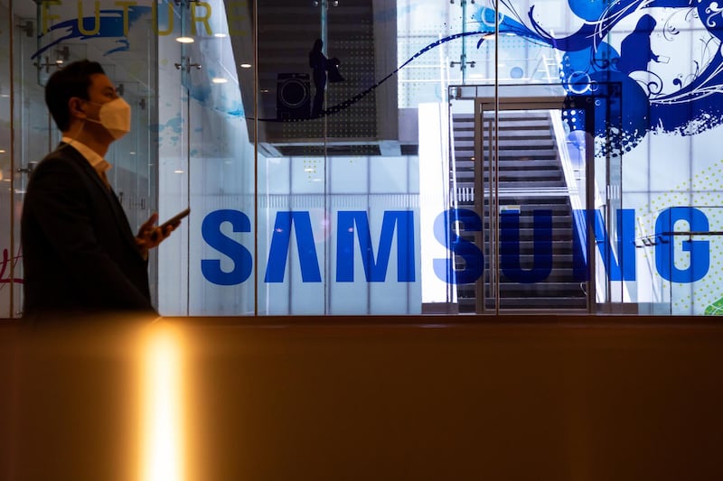 A man wearing a protective mask walks past the Samsung Electronics Co. signage at the company's D'light flagship store in Seoul, South Korea, on Tuesday, Oct. 6, 2020. Samsung were among a list of global firms that were cleared by India’s Ministry of Electronics and Information Technology that won approval to manufacture products in India under a plan aimed at attracting investment of more than 10.5 trillion rupees ($143 billion) for mobile-phone production over the next five years. Photographer: SeongJoon Cho/Bloomberg