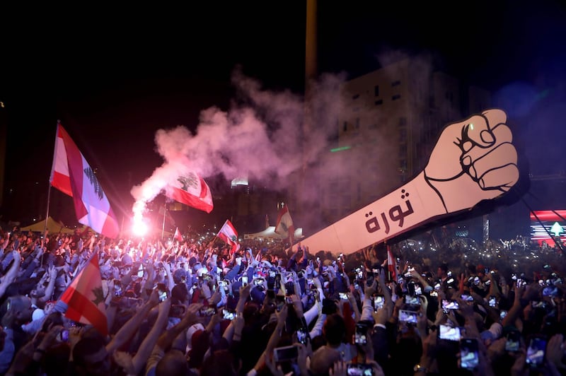 (FILES) In this file photo taken on November 22, 2019, Lebanese demonstrators raise a new giant sign of a fist that bears the Arabic word "revolution" on it, in the Lebanese capital Beirut's Martyr's Square, after the sign was burnt overnight by unknown perpetrators. Lebanon is now suffering though one of the darkest periods in its chaotic history, and soaring poverty combined with a seemingly inexorable brain drain make for a bleaker future yet. / AFP / Patrick BAZ
